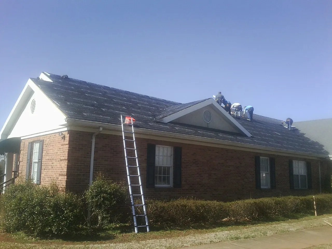 Crew tearing shingles off a brick ranch roof with a ladder set — Emergency Roof Repair work by our crew in Silverlake
