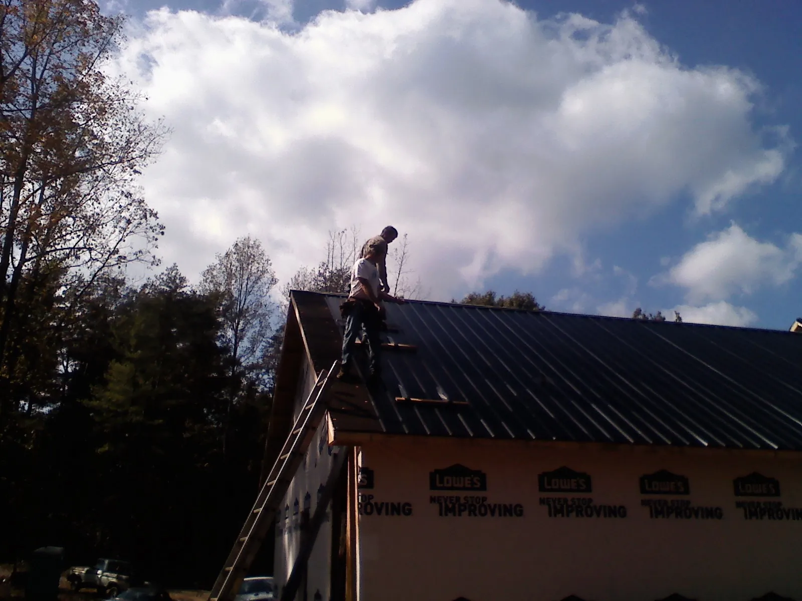 Roofer fastening dark metal panels high against a cloudy sky, from a Roof Inspection job in Silverlake