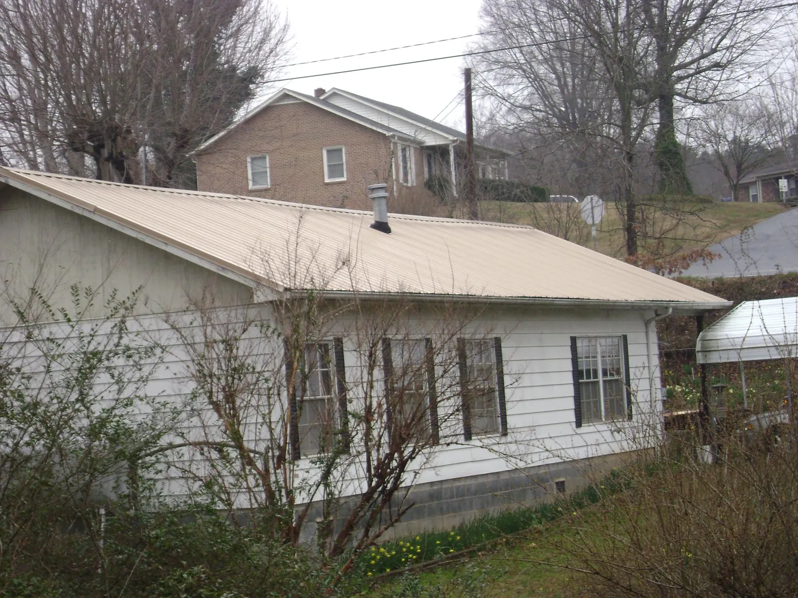 Tan metal roof on a white sided house set into a hillside — Commercial Roofing by Roofing Brothers in Silverlake